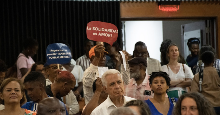 Personas asistentes a un evento del Colectivo Migración y Derechos Humanos sostienen carteles con los mensajes 'Regularizar es permitir trabajar formalmente' y 'La solidaridad es amor'.